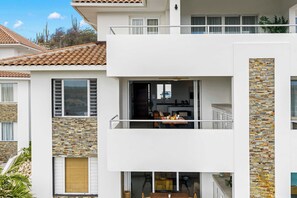 Ein modernes, zweistöckiges Gebäude mit Balkon, einer durch eine offene Tür sichtbaren Küche und einer Steinfassade.