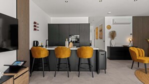 Una cocina moderna con una isla central, taburetes de bar, un televisor de pantalla plana y un área de comedor con sofá y una mesa de centro.