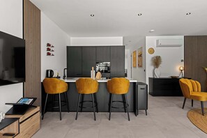 Eine moderne Küche mit Kochinsel, Barhocker, Fernseher und Essbereich mit Sofa und Couchtisch.