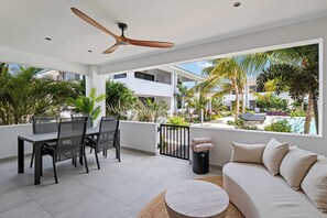 Eine moderne Terrassengaststätte mit Esstisch, Stühlen, Deckenventilator und Blick auf Pool und Grünflächen.
