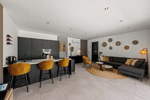 Eine moderne Küche mit einer zentralen Kochinsel, Barhocker, einem Essbereich mit einer Couch und einem Wohnzimmer mit Couchtisch.