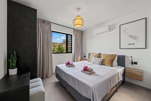 A modern hotel room with a large bed, a window with curtains, a potted plant, a wall-mounted air conditioner, and a map of Curacao. - Azure stay - Luxury Stay - Pool - Santa Rosa (Mahaai)