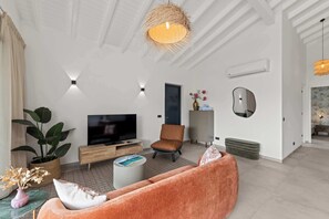 A modern living room with a flat-screen TV, a brown leather sofa, a small coffee table, and a potted plant. - Sunset Pearl Curaçao | Pool & Free Parking (Mahaai)