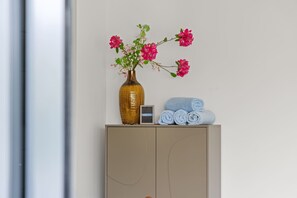 Ein beiges Sideboard mit einer Vase voller rosa Blumen und gerollten Handtüchern darauf.