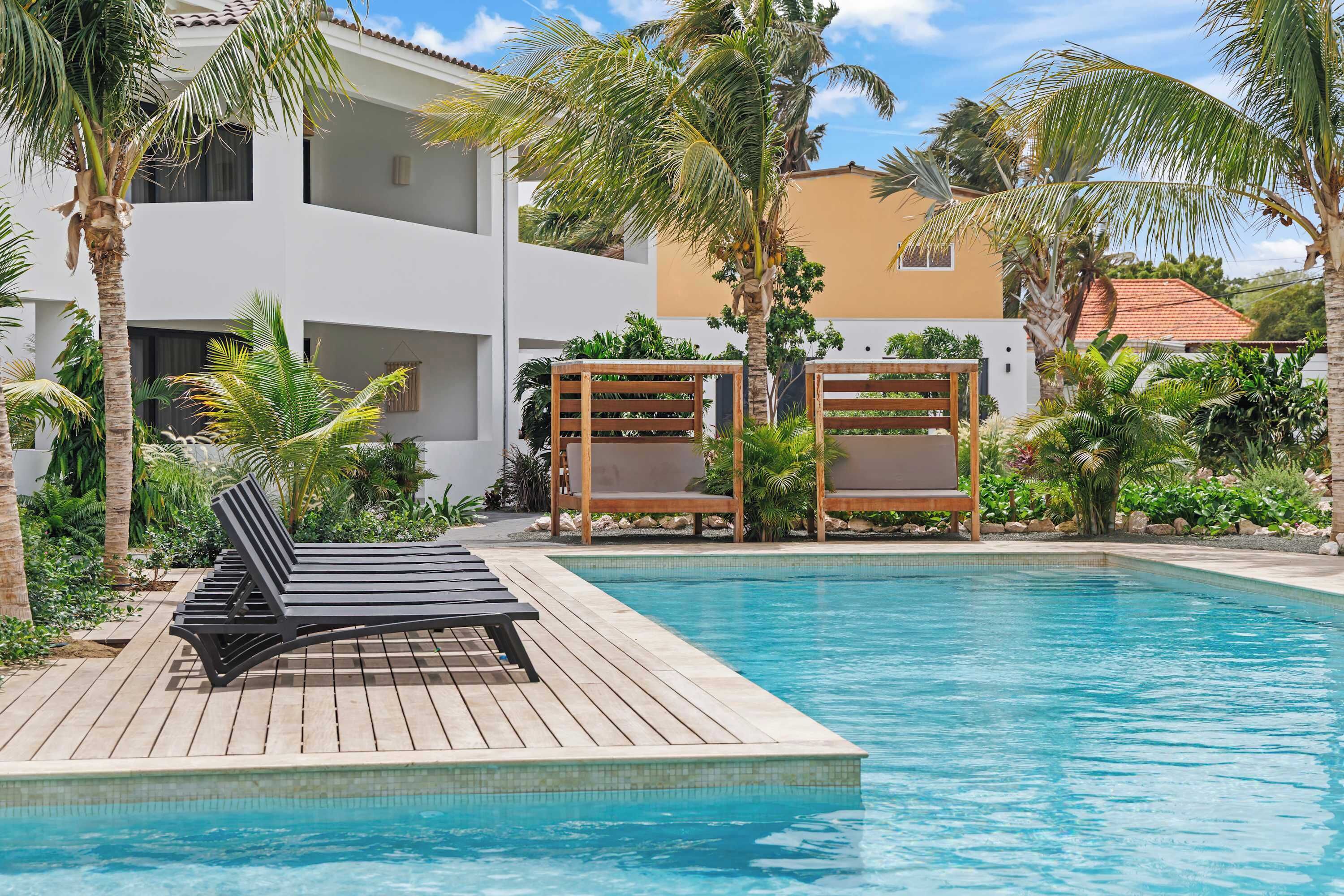 A poolside area with lounge chairs, a wooden deck, and a clear blue pool.