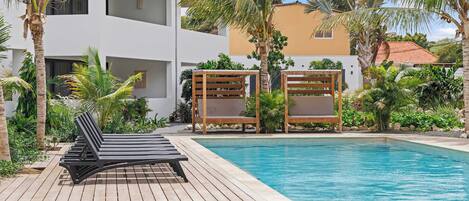 A poolside area with lounge chairs, a wooden deck, and a clear blue pool.