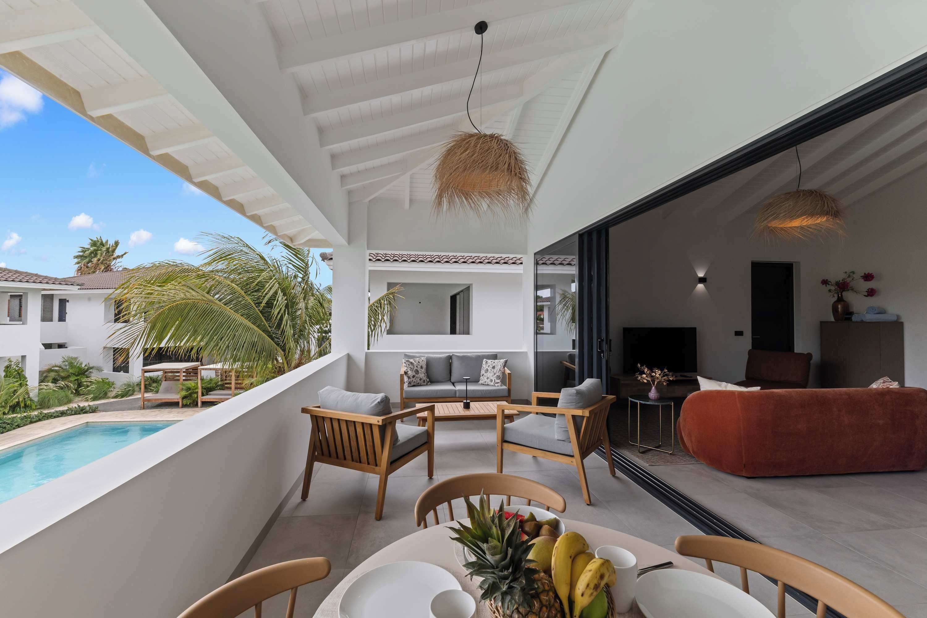 Un espacio exterior moderno con piscina, una mesa de comedor con fruta y vistas a un edificio residencial.