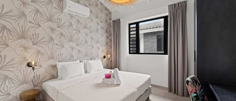 A hotel room with a bed, a bedside lamp, a wall-mounted air conditioner, a window with curtains, and a view of the outside.