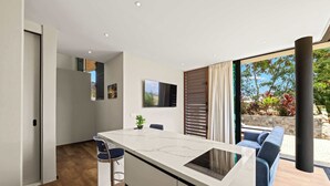 A modern kitchen with a marble countertop, a built-in oven, and a dining area with a blue chair. - Villa Azure Fairways- luxury villa at Bluebay (Bluebay)