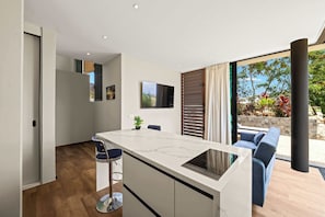 A modern kitchen with a marble countertop, a built-in oven, and a dining area with a blue chair. - Villa Azure Fairways- luxury villa at Bluebay (Bluebay)
