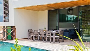 An outdoor dining area with a pool, wooden deck, and modern furniture. - Villa Azure Fairways- luxury villa at Bluebay (Bluebay)