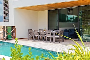 An outdoor dining area with a pool, wooden deck, and modern furniture. - Villa Azure Fairways- luxury villa at Bluebay (Bluebay)