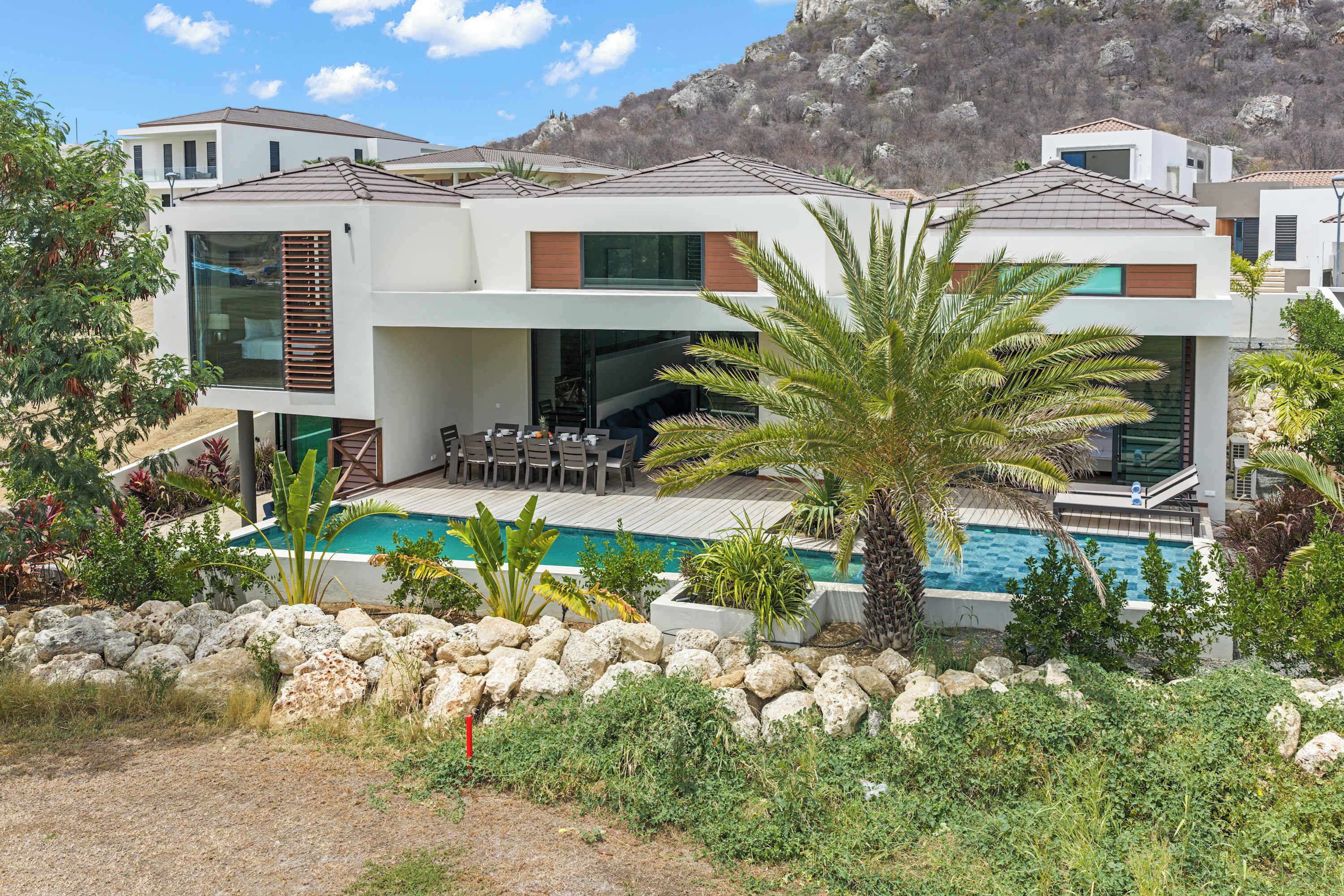 Une maison moderne à deux étages, dotée d’une piscine, d’un espace extérieur aménagé et offrant une vue sur un paysage montagneux.