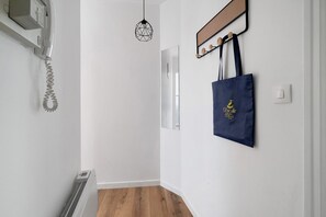 Un couloir avec un radiateur, un luminaire suspendu et un porte-manteau fixé au mur, sur lequel est accroché un sac.