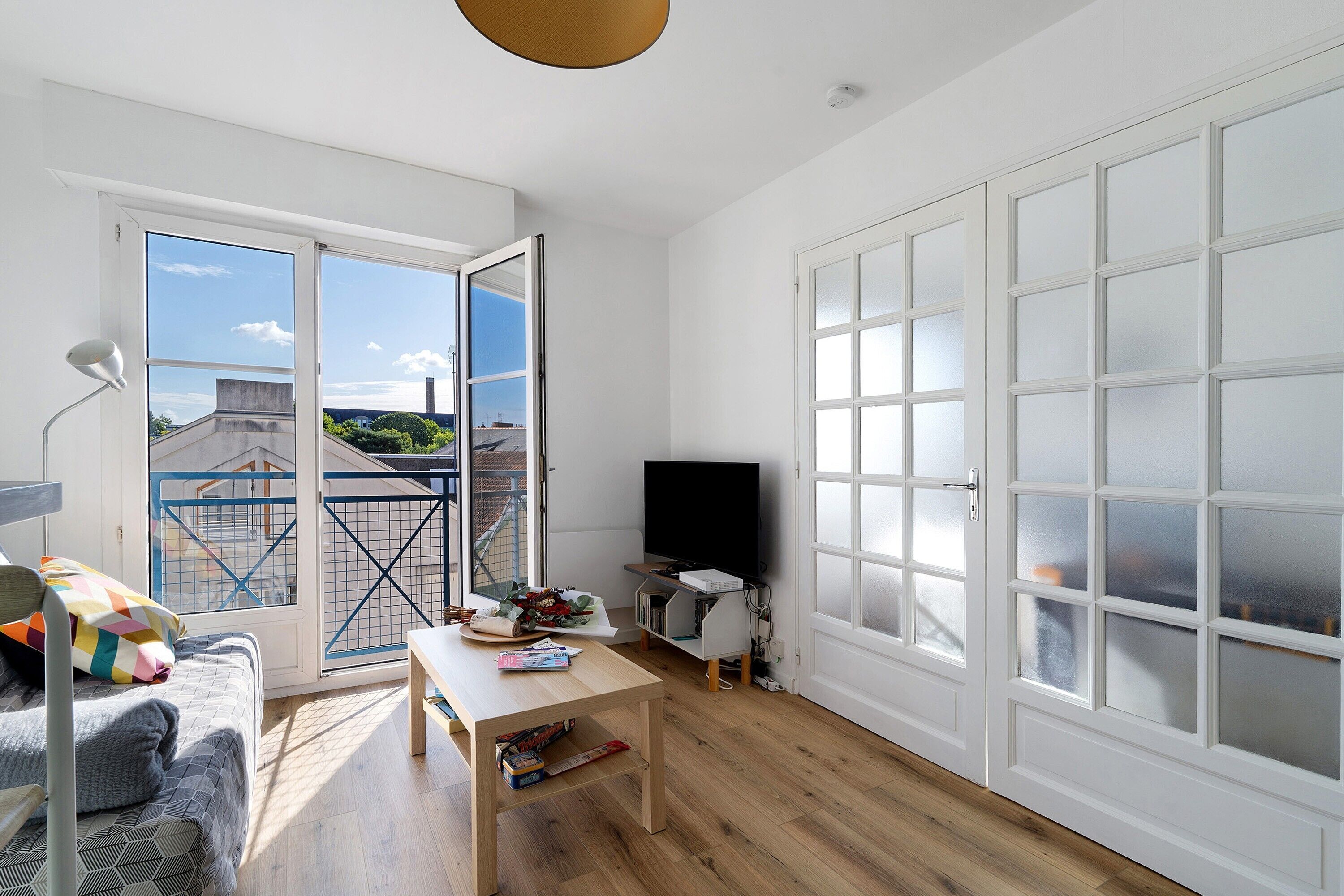 Ein helles Wohnzimmer mit großem Fenster, einem Flachbildfernseher, einem Holztisch und einer Couch.