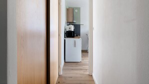 Ein schmaler Flur führt zu einer Küche mit einem weißen Kühlschrank, einer Mikrowelle und einem Holzschrank.