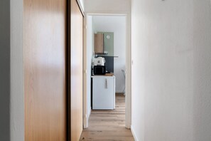 En smal hall leder in till ett kök med ett vitt kylskåp, en mikrovågsugn och ett träskåp.