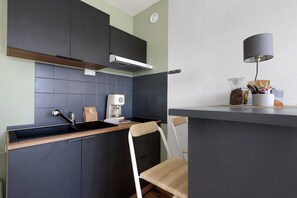 Une cuisine compacte avec des meubles de rangement sombres, une cuisinière encastrée et une machine à café.