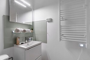 Une salle de bain moderne avec un lavabo blanc, un miroir et un porte-serviettes.
