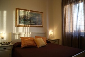 A hotel room with a bed, two bedside tables, a painting on the wall, and a window with curtains.
