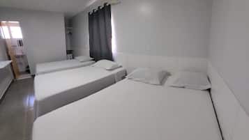 Habitación de hotel con tres camas, baño y aire acondicionado.