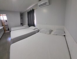 Habitación de hotel con tres camas, baño y aire acondicionado.