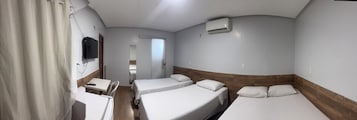Habitación de hotel con dos camas individuales, un escritorio, una silla, un televisor y aire acondicionado.