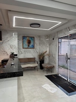 Un interior moderno con una pared de mármol, un mostrador de recepción, un sofá, una silla y una puerta que da al exterior.