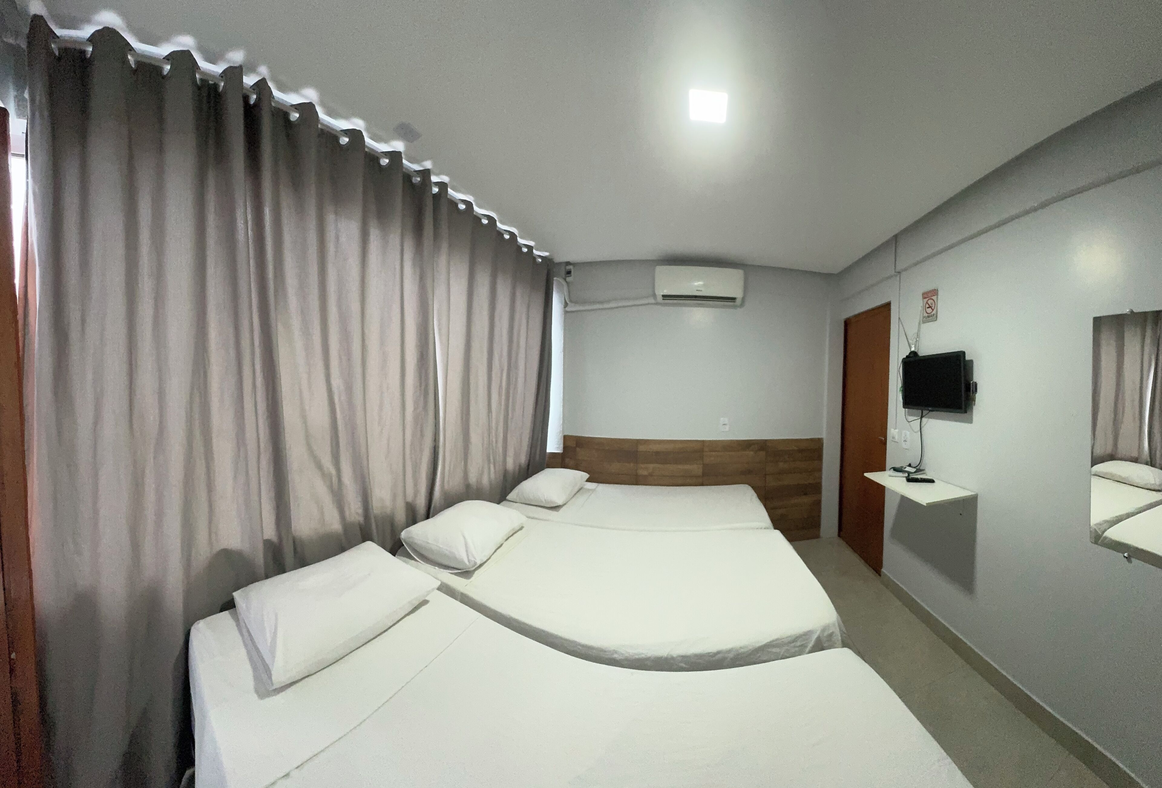 Ein Hotelzimmer mit zwei Betten, einem Fernseher, einer Klimaanlage und einem kleinen Schreibtisch mit Spiegel.