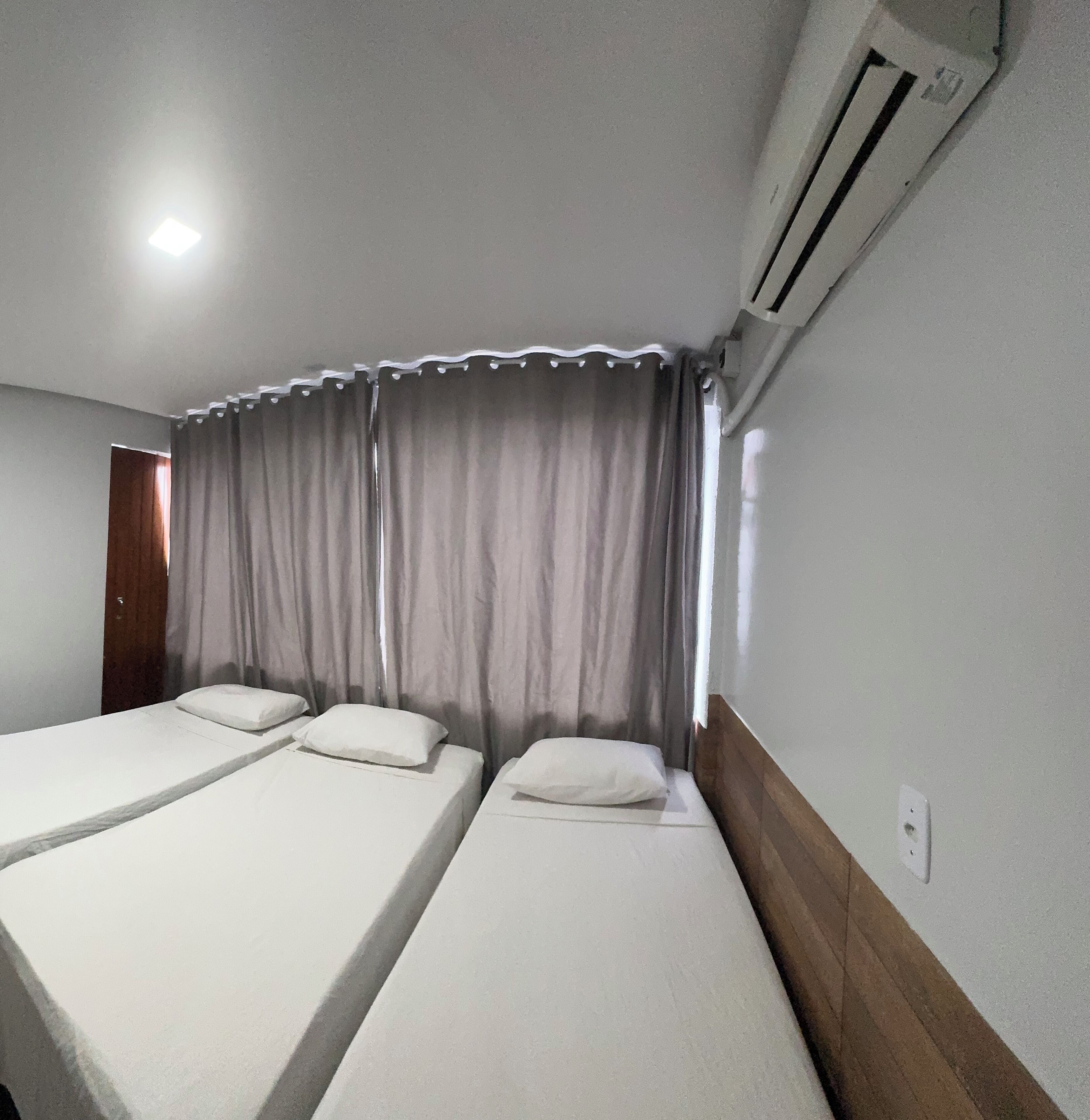 A room with two single beds, a wooden headboard, a window with curtains, and an air conditioning unit.