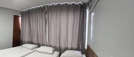 A room with two single beds, a wooden headboard, a window with curtains, and an air conditioning unit.