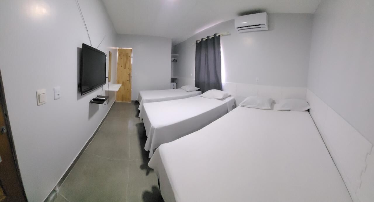 A hotel room with three single beds, a flat-screen TV, a small table, and a door leading to another room.
