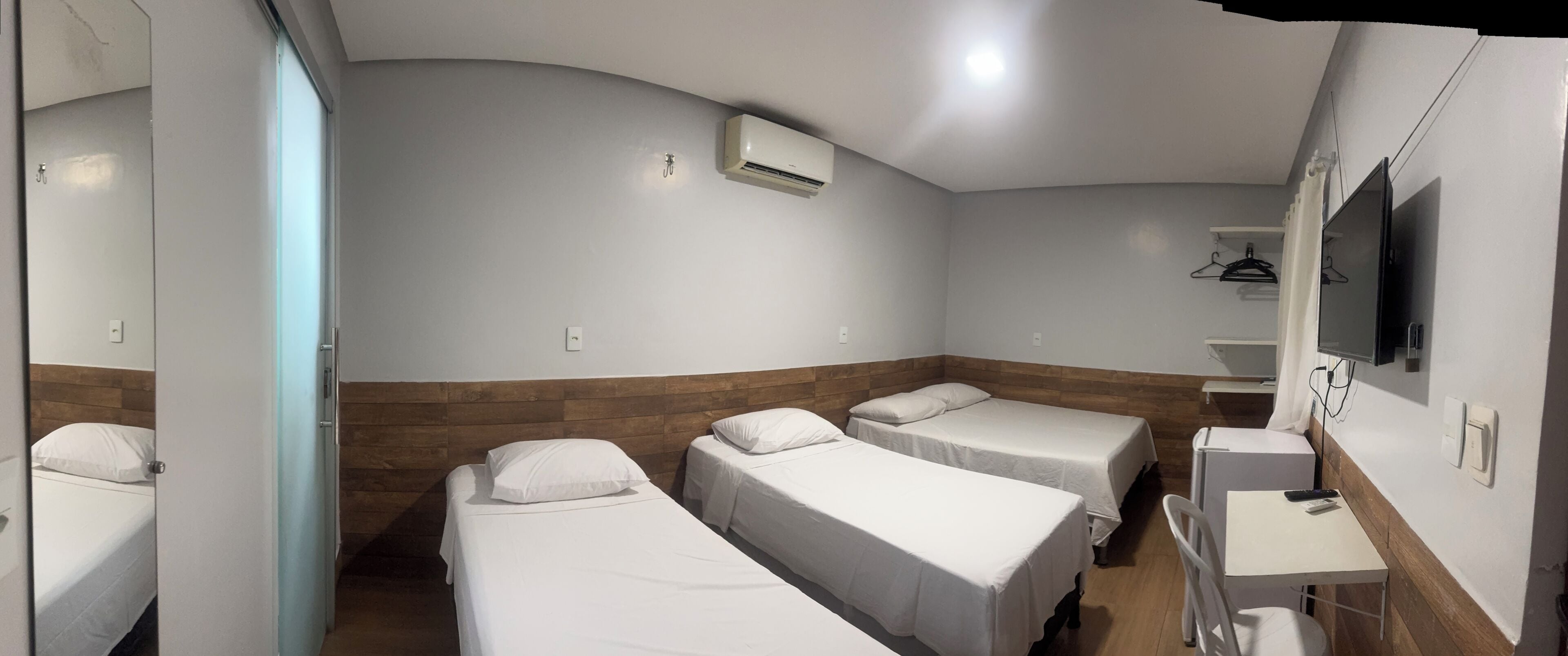 Habitación de hotel con tres camas individuales, un escritorio pequeño, un espejo y un aire acondicionado.