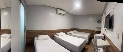 Habitación de hotel con tres camas individuales, un escritorio pequeño, un espejo y un aire acondicionado.