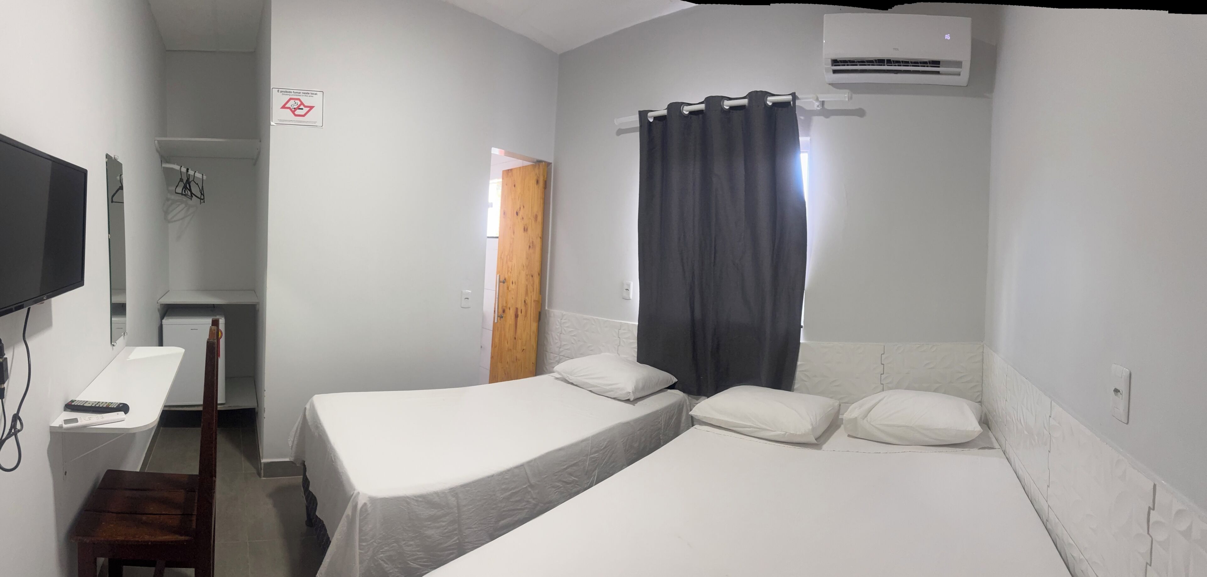 A hotel room with a bed, a desk, a television, and an air conditioning unit.