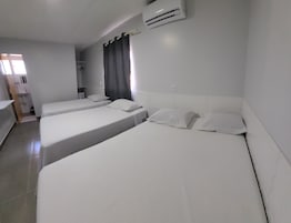 A hotel room with three single beds, a bathroom, and a window with curtains.
