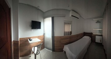 A compact room with a bed, a small table, a chair, a TV mounted on the wall, and a window with curtains.