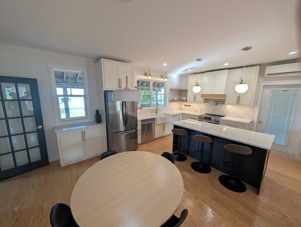 A modern kitchen with white cabinetry, stainless steel appliances, a central island with bar stools, and a dining table.