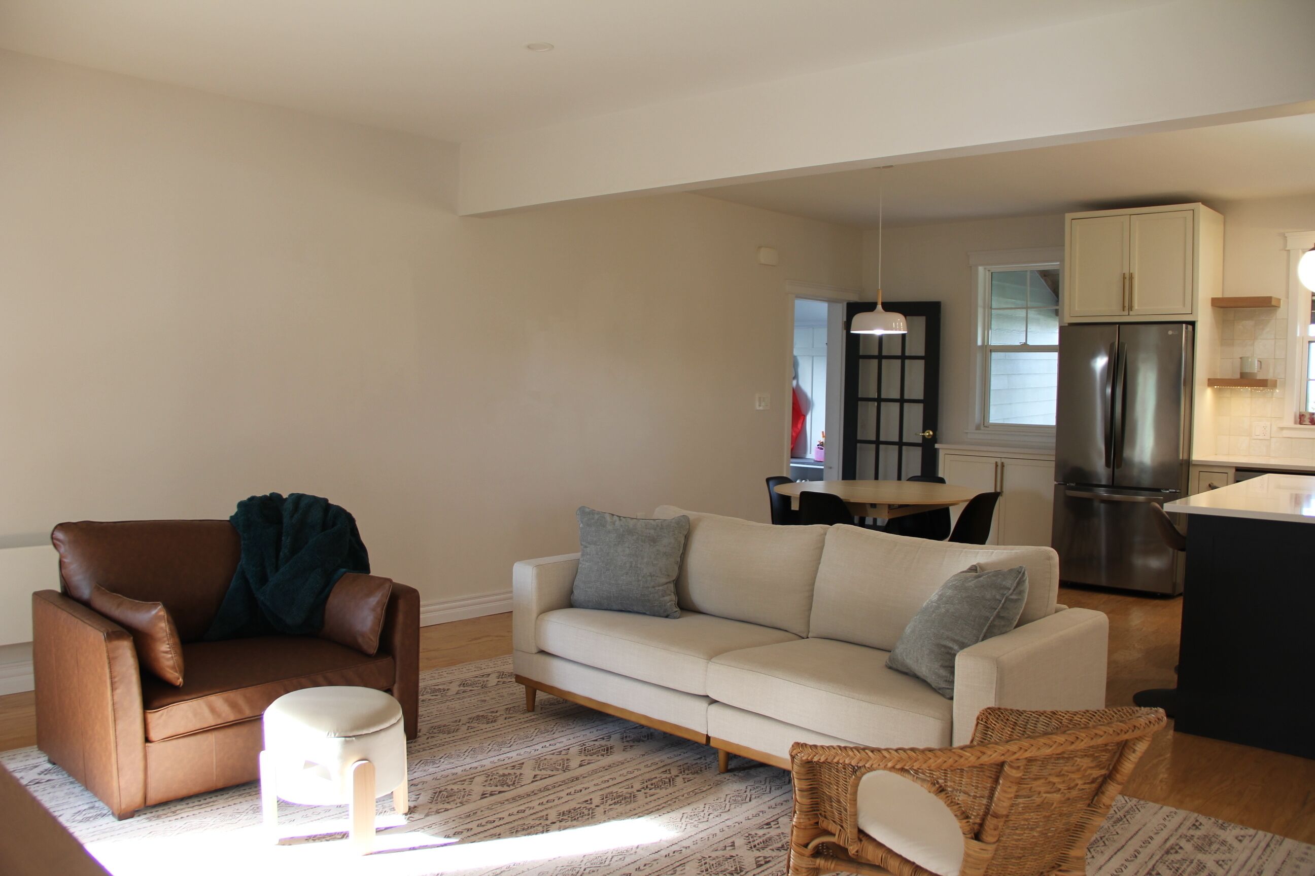 A living room with a brown leather chair, a white sofa, and a small stool. There is a dining table with chairs in the background.