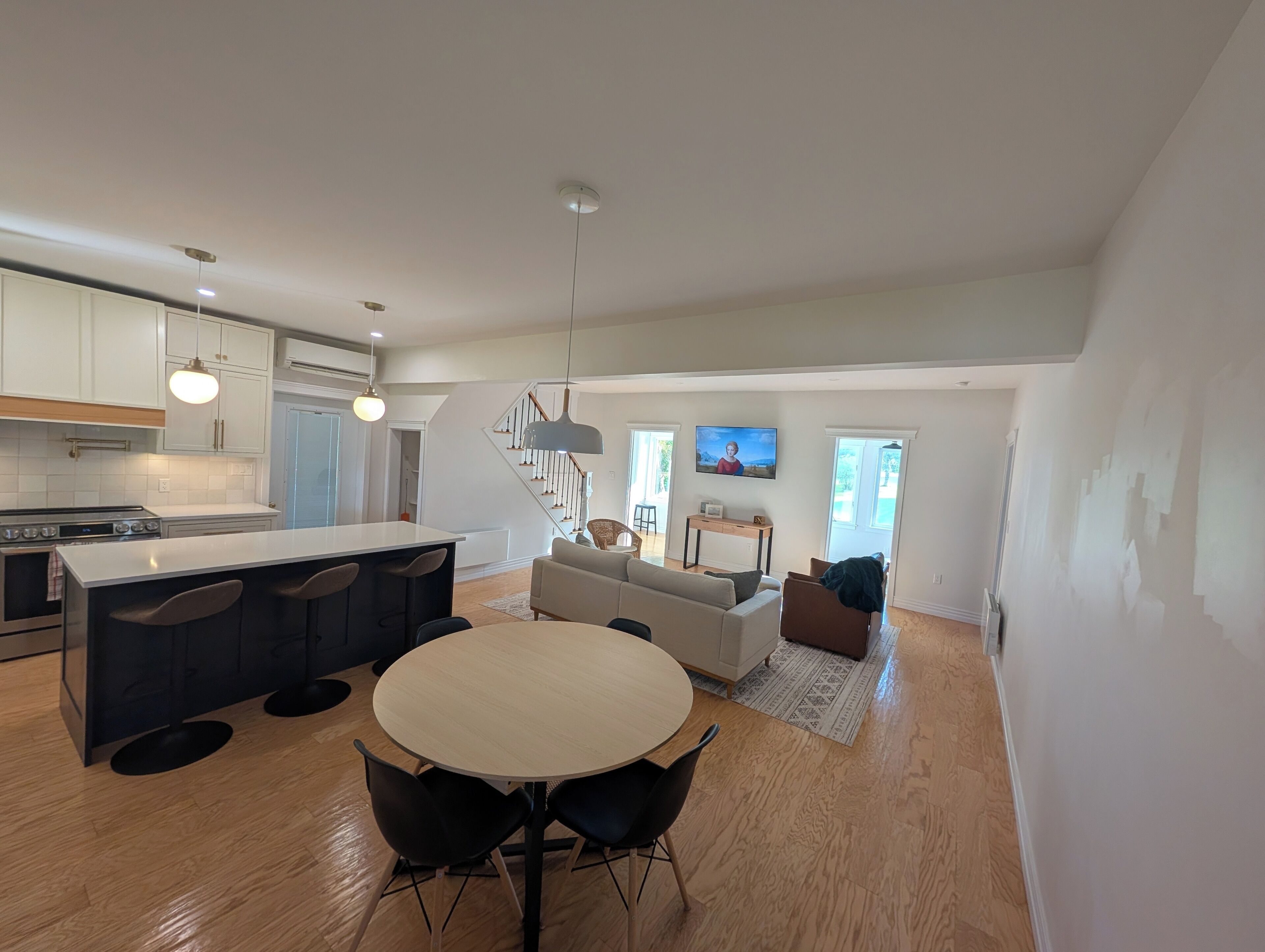 A modern kitchen with a central island, dining area with a round table and chairs, and a living room with a sofa and a TV.