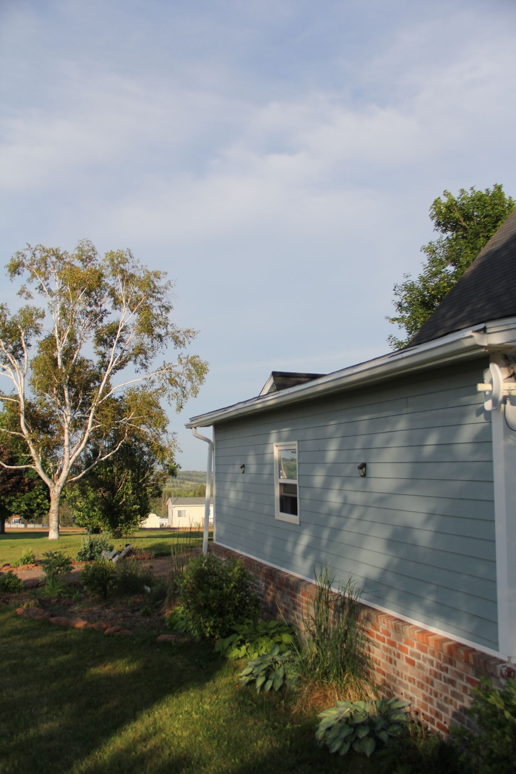 A residential house with a brick foundation and a grey siding exterior.