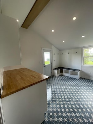 A kitchen with a wooden countertop, white cabinets, a bench, and a patterned floor.