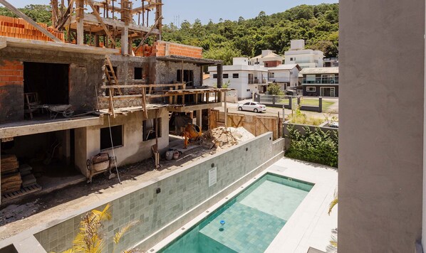 A construction site with a swimming pool, wooden scaffolding, and a partially built brick structure. - Comfortable Studio 750m From Praia de Canas Tps210 (Florianópolis)