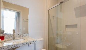 A bathroom with a glass shower enclosure, a sink with a marble countertop, and a window with curtains. - Comfortable Studio 750m From Praia de Canas Tps210 (Florianópolis)