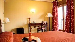 Een hotelkamer met een bed, een bureau, een stoel, een lamp en een televisie aan de muur.