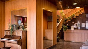 Een receptie met een piano, een trap met planten en een houten wand.