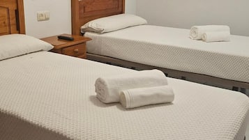 Habitación de hotel con dos camas individuales, cada una con cubrecama blanco texturizado y toallas enrolladas blancas.