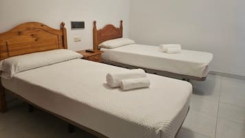 Dos camas individuales con cabeceros de madera, sábanas blancas y un control remoto sobre la mesita de noche.
