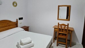 Une chambre à coucher avec un lit, une chaise en bois, un bureau et un miroir au mur.