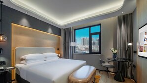 Moderni hotellihuone, jossa on suuri sänky, työpöytä, tuoli ja näkymä kaupungin ylle.
